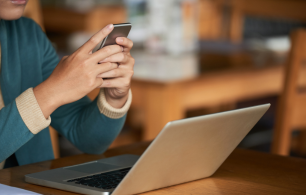 Lady using her phone in front of her laptop.